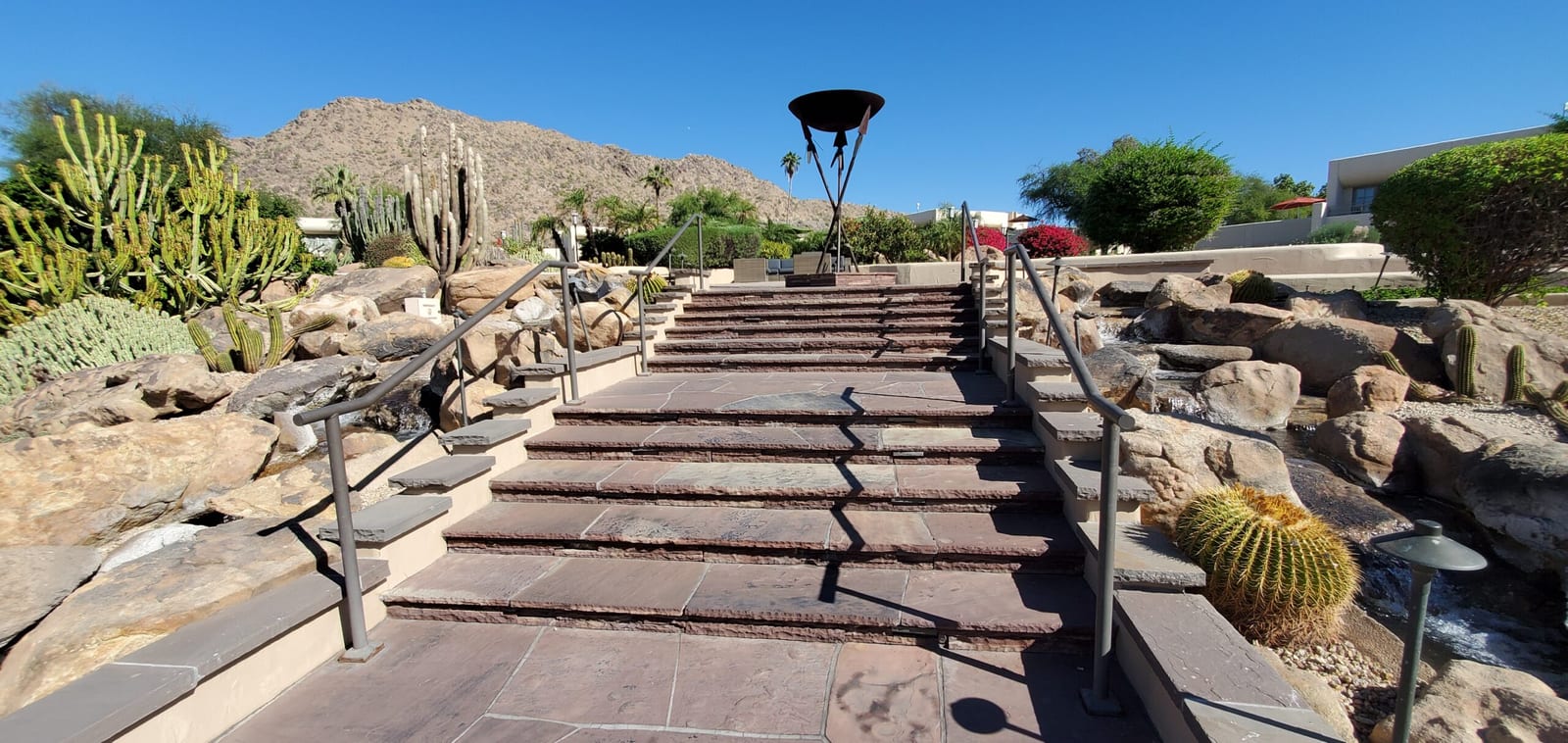 Grand sandstone stairway with cascading waterfalls, organ pipe cacti, and iconic fire torch. Grand sandstone staircase flanked by boulder waterfalls and iron fire torch