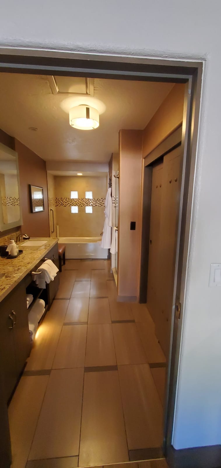 View across the bathroom suite toward the freestanding soaking tub beneath frosted glass block windows. Perspective view from the bathroom vanity toward the deep soaking tub