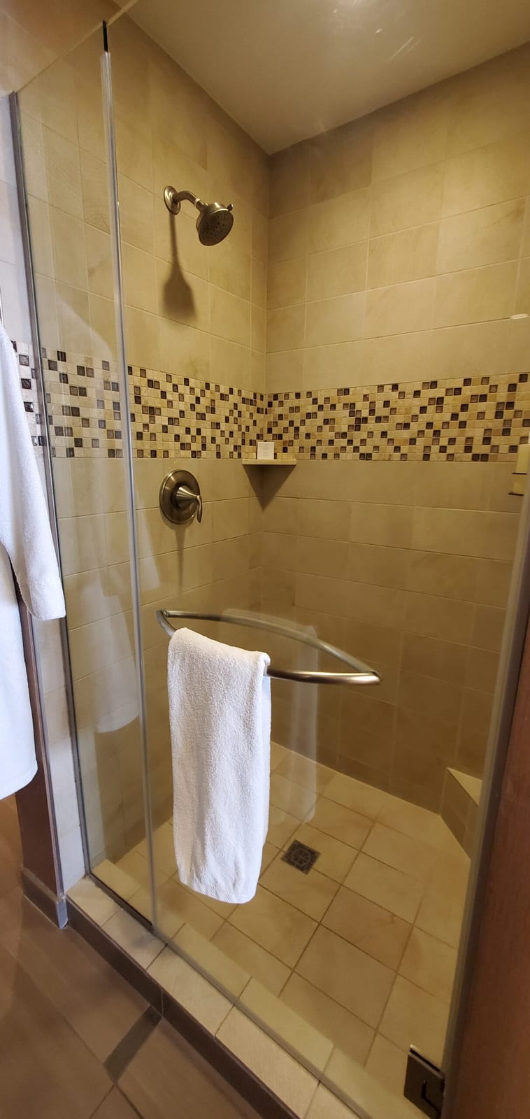 Walk-in glass shower enclosure lined in natural travertine stone and mosaic accents. Travertine walk-in shower with mosaic tile border